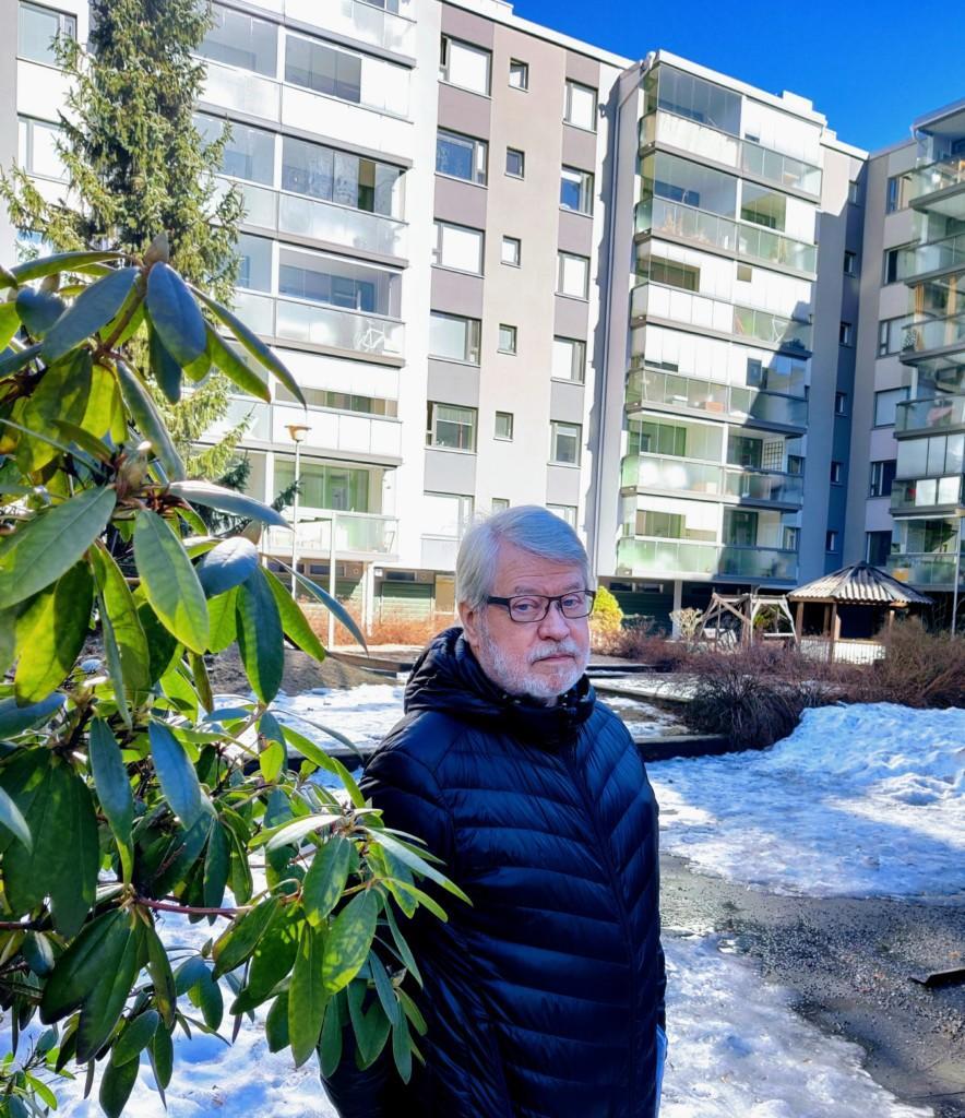 Asunto-osakeyhtiön pihalla otettu kuva, jossa näkyy kerrostalo ja asunto-osakeyhtiön hallituksen puheenjohtaja Matti Lehtonen.